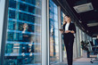 © BullRun - Caucasian female entrepreneur dressed in formal wear going near panoramic window in office, confident business woman with modern digital tablet looking away during working day in enterprise