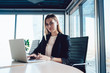 © BullRun - Portrait of blonde female manager sitting at working table with laptop computer typing and sending business emails,confident intelligent formally dressed woman looking at camera during working process