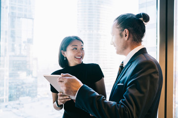 Wall Mural - Happy caucasian male and female colleagues discussing news from social networks using digital tablet for browsing, successful woman and man business partners satisfied with cooperation results