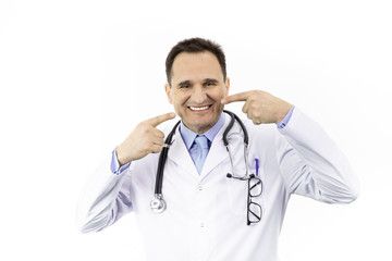 Close up portrait of happy with snow-white smile adult male doctor pointing on her perfect clear white teeth, isolated on white background. Physician in medical gown with stethoscope over neck.