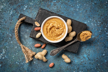 Tasty peanut paste in white bowl and vintage spoon with raw nuts