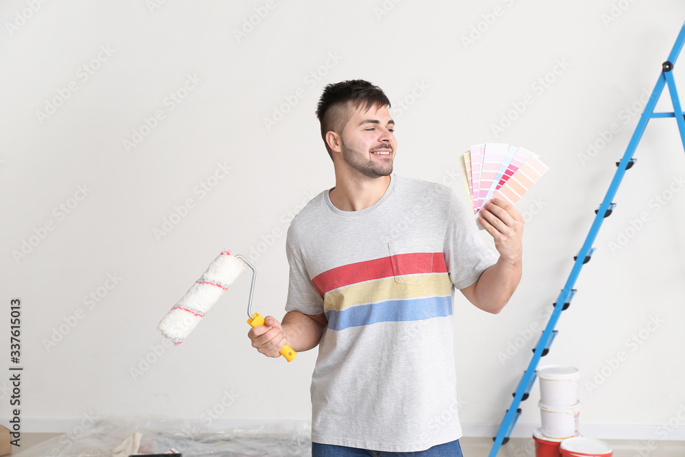 Young man with color swatches and paint roller indoors