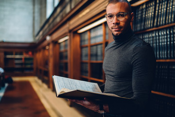 Wall Mural - Half length portrait of intellectual professor of history in bifocal eyewear looking at camera while holding literature book in hand for making research of information for new science publication