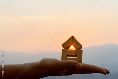 Cuadros en Lienzo Hands holding house sunset background, Real estate investment is a business to build a house to sell to buyers in the market through agents