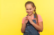 © khosrork - Portrait of sneaky scheming little girl in denim overalls thinking over cunning prank and smirking, disobedient child having sly tricky plans in mind. indoor studio shot isolated on yellow background