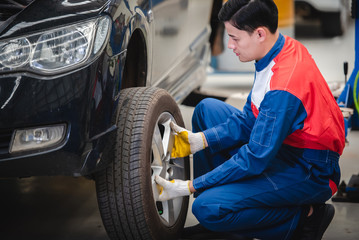 Asian car mechanic is removing the wheel and checking the brakes and suspension in the car service with a forklift. Repair and maintenance center