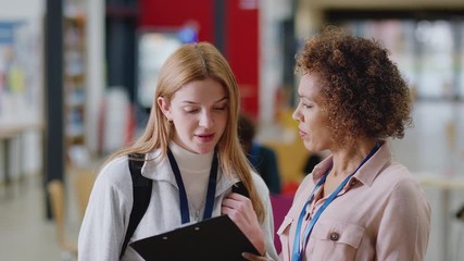 Wall Mural - Dolly shot of female college student meeting with woman tutor in busy communal campus building - shot in slow motion