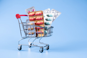 Wall Mural - Medicine, vitamins and antioxidant supplements in trolley or shopping cart on blue background