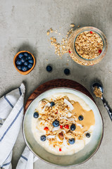 Wall Mural - Morning healthy breakfast bowl with yogurt, muesli, blueberry, banana, coconut on the concrete background. Top view. Flat lay