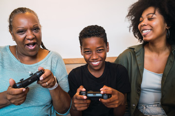 Grandmother, mother and son playing video games at home.