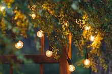 Close-up Of An Electric Lamp, A Garland On A Wedding Arch In The Evening