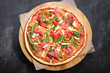 Pizza on wooden board on black stone background. Italian traditional food. Delicious pizza with serrano jamon, parmigiano-reggiano cheese and rucola. Restaurant menu. Copy space, top view