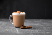 Side View Of Delicious Cappuccino Coffee With Milk Foam Sprinkled With Cinnamon In A Transparent Glass Mug On A Gray Background, Horizontal Format