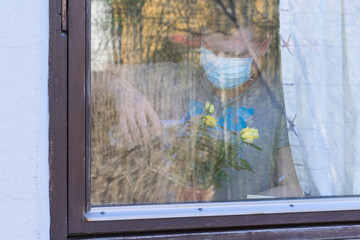 A man near the window looking wotering yellow pot rose.