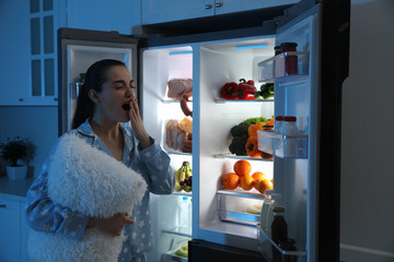 Canvas Print - Young woman with pillow near open refrigerator at night