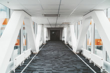 Bright Long Modern Passageway Between Two Towers Of An Office Or A Hospital Skyscraper With  Zig-zag Lines Of The Load-bearing Beams, Suspended Ceiling, Heating Batteries, And Carpeting On The Floor