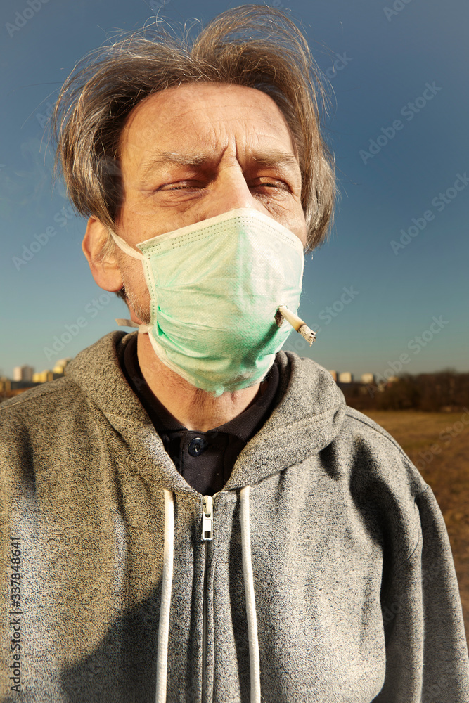 Man smoking through his face mask in sunny day on public Stock Photo