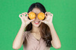 © tuaindeed - Funny cheerful young Asian woman holding two oranges on her eyes over green isolated background.