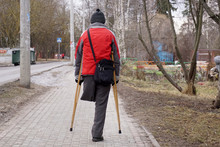    A Man On One Leg, With Two Crutches, Is Walking Along The Sidewalk.