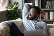 Smiling peaceful handsome african american guy relaxing on comfy sofa with laptop, looking away at window, thinking of opportunities, remembering good life moments, visualizing future at home.
