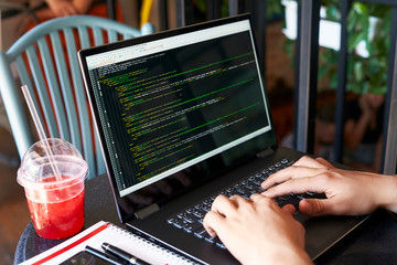 Developer programmer with laptop. Program code and script data on screen. Young freelancer in glasses working on project in cafe. Back view over the shoulder shot