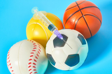 Different balls and syringe on blue background. Concept of doping in professional sport. Rehabilitation, treatment after competition. Illegal medicaments using on tournament