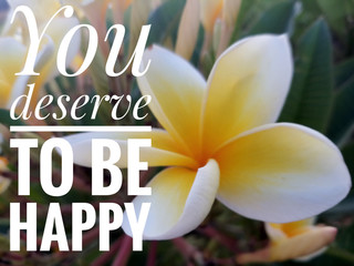 Inspirational quote - You deserve to be happy. On background of beautiful white and yellow Bali frangipani flower plant blossom. Self care and happiness concept.