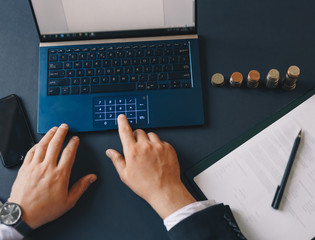 Hand businessman holding coins stack  and using laptop to calculate. Concept saving money and finance accounting. Top view.