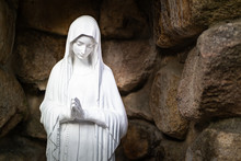 A Praying Statue Of The Virgin Mary In A Stone Background.