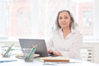 © Seventyfour - Portrait of successful senior businesswoman looking at camera while using laptop sitting in white office against window, copy space