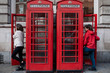 Couple of women in typical London phone booths in the morning. One of them in a light sweater goes into the phone booth while the other in a red coat comes in to make a call.