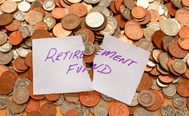 The words retirement fund written in purple pen on white paper on top of a pile of British coins