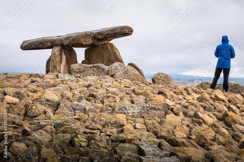 Cuadros en Lienzo Hiker dressed with a blue jacket beholding the landscape next to the dolmen La