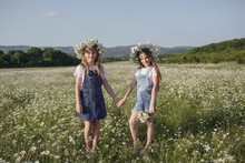 Two Cute Teen Girls In Denim Overalls Walk In A Daisy Field