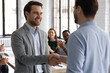 Smiling male business partners handshake at office meeting close deal or make agreement, excited businessman shake hand of worker congratulate with job achievement or promotion at briefing