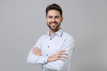 Canvas Print - Smiling successful young unshaven business man in light shirt posing isolated on grey background studio portrait. Achievement career wealth business concept. Mock up copy space. Holding hands crossed.