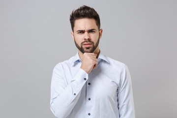 Canvas Print - Puzzled young unshaven business man in light shirt posing isolated on grey wall background studio portrait. Achievement career wealth business concept. Mock up copy space. Put hand prop up on chin.