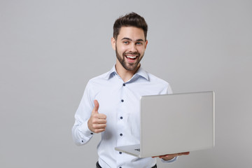 Wall Mural - Cheerful young unshaven business man in light shirt isolated on grey wall background. Achievement career wealth business concept. Mock up copy space. Working on laptop pc computer, showing thumb up.