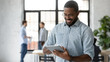 © fizkes - Smiling African American male employee use modern tablet gadget with wireless Internet connection at workplace, happy confident biracial man worker texting or messaging on Pad device in office