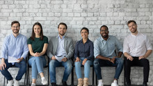 Portrait Of Smiling Diverse Multiracial Young People Sit In Row On Chairs Wait For Office Interview, Happy Motivated Multiethnic Job Candidates Hired For Vacant Work Position, Employment Concept