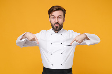 Wall Mural - Amazed young bearded male chef cook or baker man in white uniform shirt posing isolated on yellow background studio portrait. Cooking food concept. Mock up copy space. Pointing index fingers down.