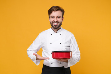 Wall Mural - Smiling young bearded male chef cook or baker man in white uniform shirt posing isolated on yellow background. Cooking food concept. Mock up copy space. Pointing hand on metal baking form for pie.