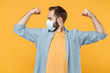 Strong young man in sterile face mask posing isolated on yellow background studio portrait. Epidemic pandemic spreading coronavirus 2019-ncov sars covid-19 flu virus concept. Showing biceps, muscles.