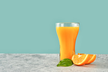 Wall Mural - Glass of fresh orange juice with oranges on green-blue background