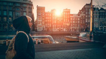 Cute young woman walks along water canal in Amsterdam at sunset sunlight, Netherlands. European travel concept.