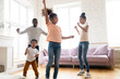 © fizkes - Happy loving young african american family dancing to favorite song at home. Smiling dad and mom teaching young girl and boy modern style. Having fun together with two cute little kids in living room