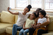 © fizkes - African American parent with two kids taking selfie, smiling woman holding phone, happy husband with son and daughter posing for photo with wife, family having fun together with gadget.