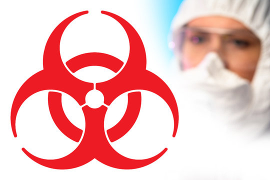 A large red biohazard sign and the face of a chemist in a protective mask. Medical quarantine. Security measures during quarantine. Preventing the spread of the disease. Epidemic.