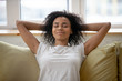 © fizkes - Rest african american woman with hands behind head relaxing at home. Smiling calm successful girl stretching during break at living room after work done, satisfied by good result.