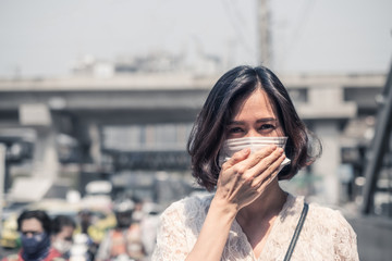 Asian woman wearing mask for prevent dusk pm 2.5 bad air pollution and coronavirus or covid-19 having headache, fever. Girl wears mask due to bad smell and prevent virus infection from people in city.